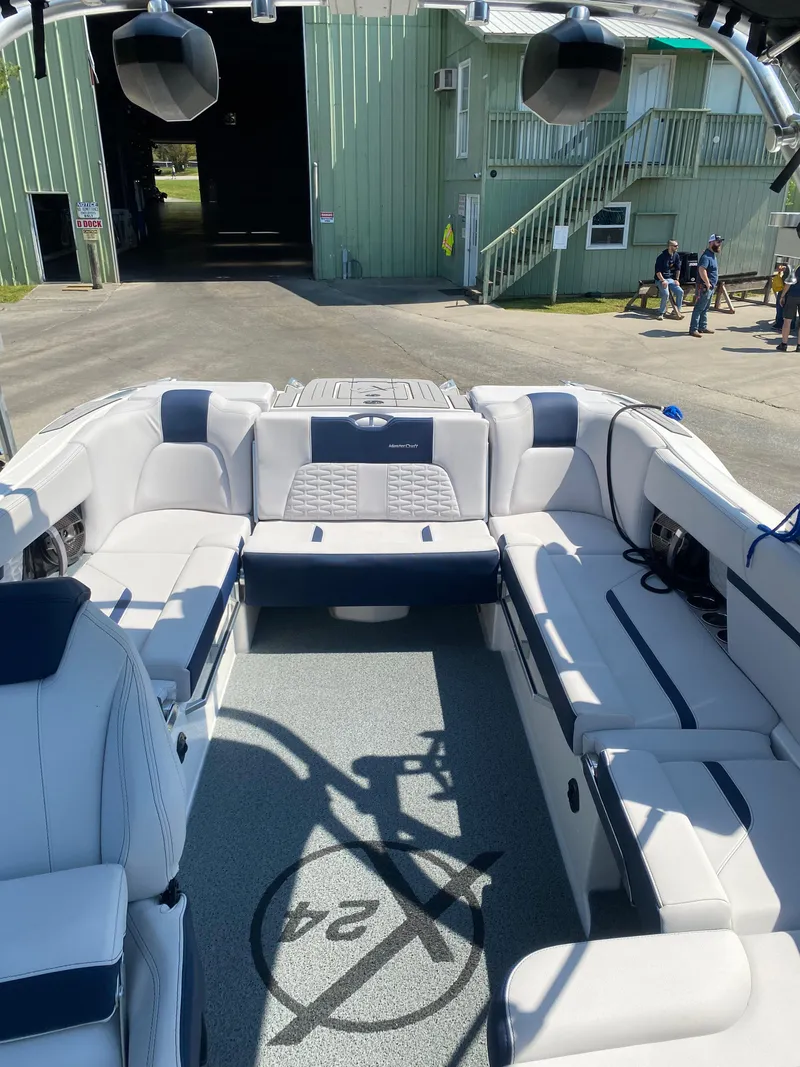 Slide: The Image of 2021 MasterCraft X24 boat interior with white and blue seating, docked near a green building. - 5