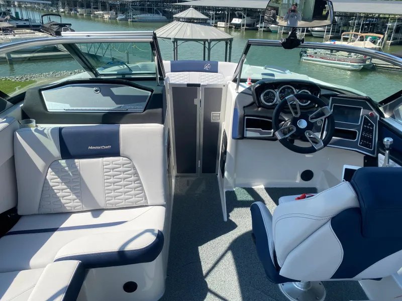 Slide: The Image of 2021 MasterCraft X24 boat interior with modern dashboard and seating, docked by the water. - 9