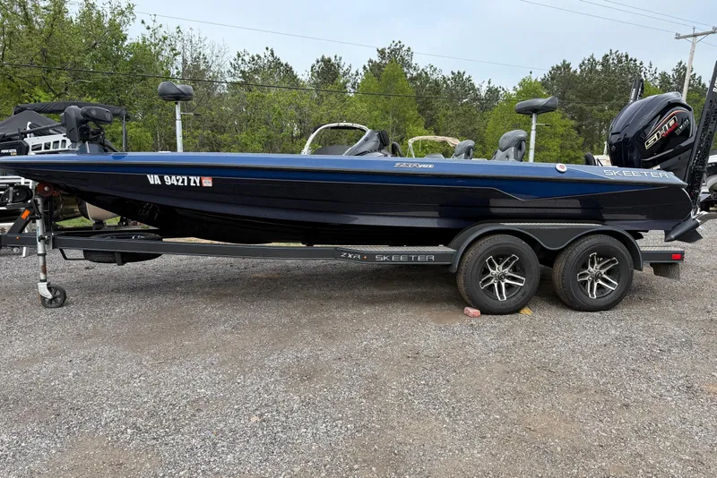 Slide: The Image of 2023 Skeeter ZXR20 boat on trailer, parked outdoors with trees in background. - 13