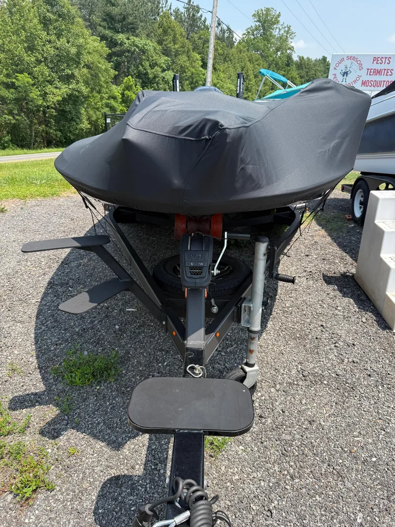 Slide: The Image of 2023 Skeeter ZXR20 boat covered, parked on gravel with greenery in the background. - 28