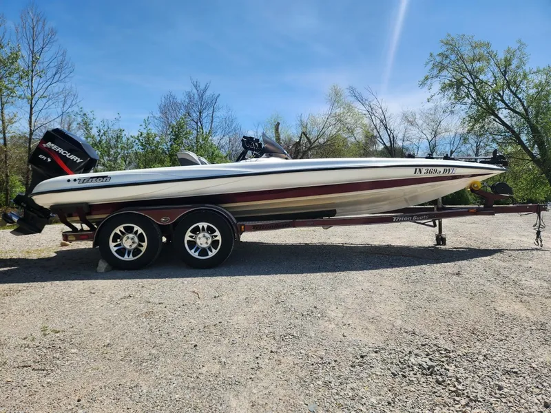 Slide: The Image of 2000 Triton TR21 boat on trailer, parked outdoors on gravel, with trees in background. - 0