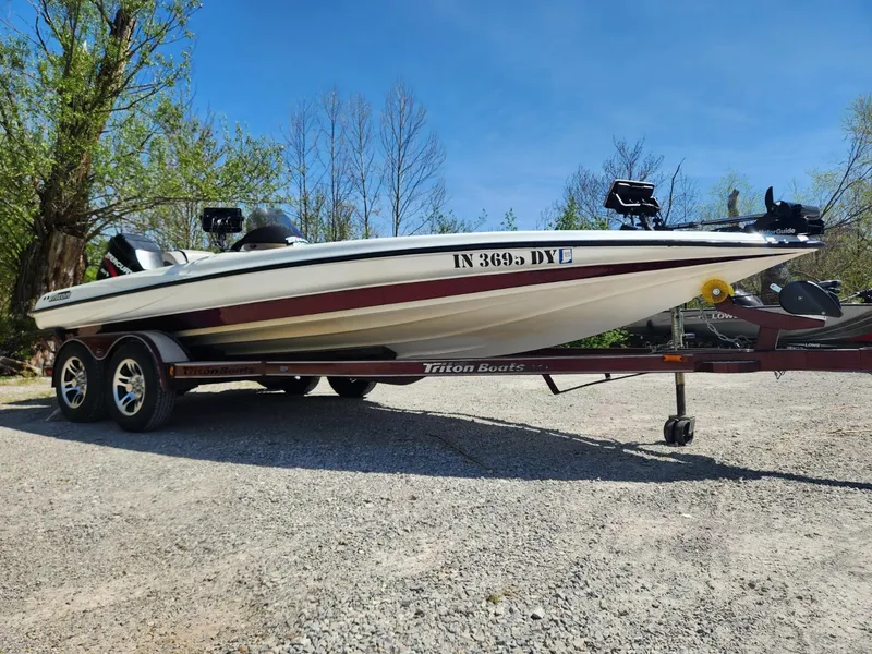 Slide: The Image of 2000 Triton TR21 boat on trailer, parked outdoors on gravel, under clear blue sky. - 2