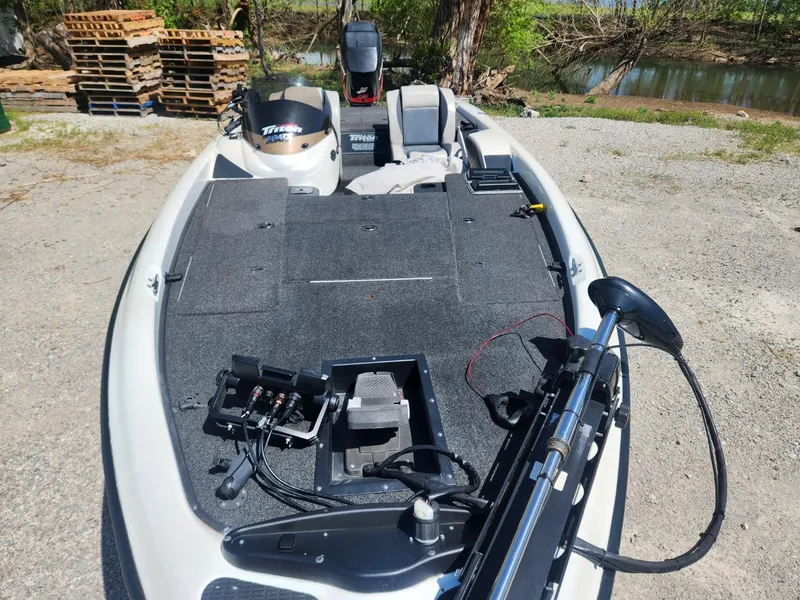 Slide: The Image of 2000 Triton TR21 fishing boat with trolling motor and spacious deck, parked near a lake. - 3