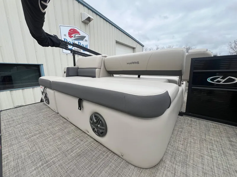 Slide: The Image of 2022 Harris Cruiser 230 boat interior with cushioned seating and speakers, docked near a building. - 22
