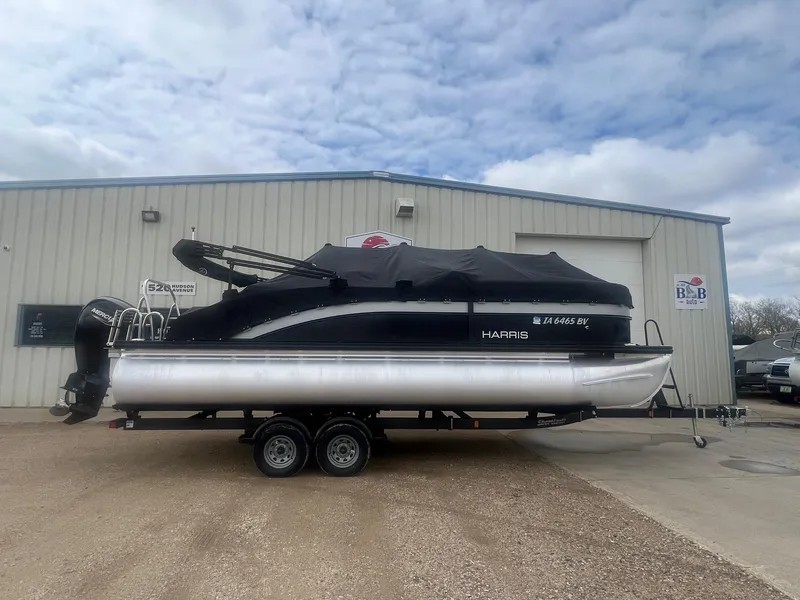 Slide: The Image of 2022 Harris Cruiser 230 pontoon boat on trailer, parked outside a building under cloudy sky. - 29