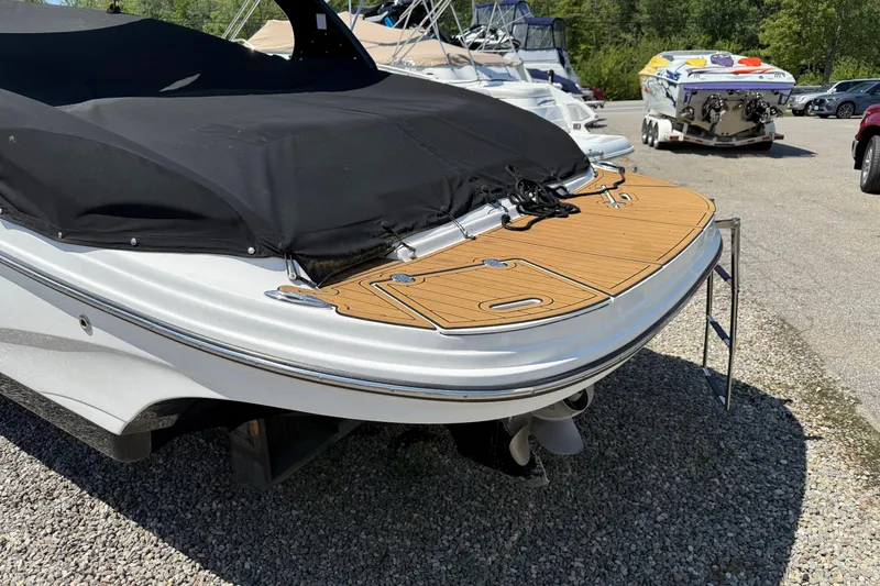 Slide: The Image of 2015 Rinker 246 Bowrider with covered deck and swim platform, parked on gravel. - 11