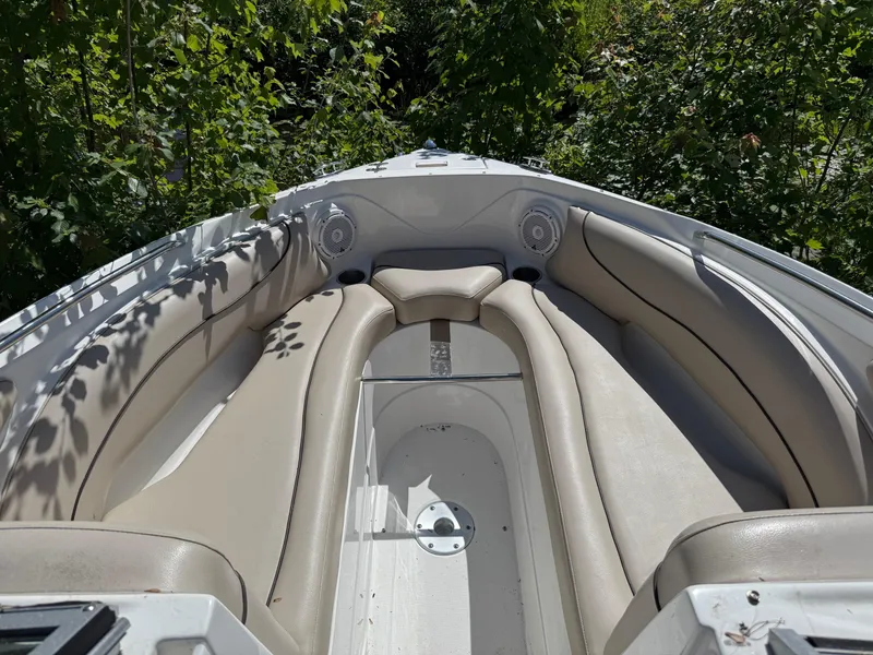Slide: The Image of 2015 Rinker 246 Bowrider boat interior with beige seating and lush greenery background. - 7