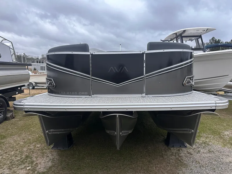 Slide: The Image of 2025 Avalon LSZ Cruise Rear Bench pontoon boat, gray exterior, parked on grass under cloudy sky. - 1