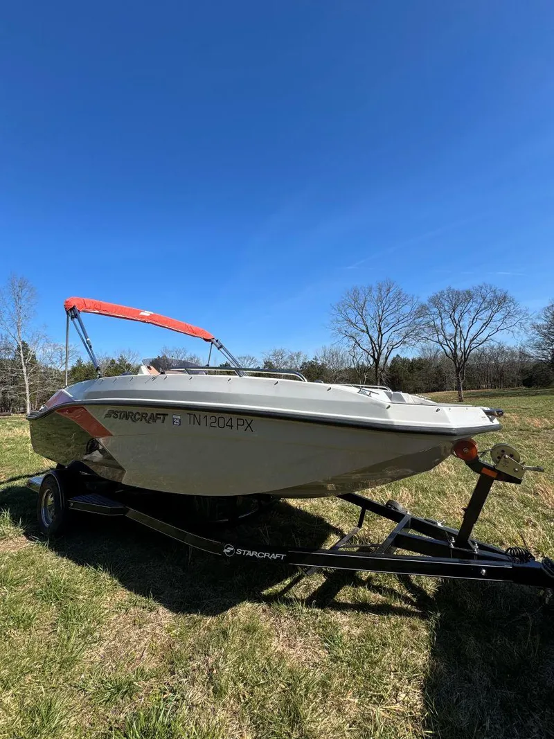 Slide: The Image of 2022 Starcraft SVX 171 OB boat on trailer, parked on grassy field under clear blue sky. - 2