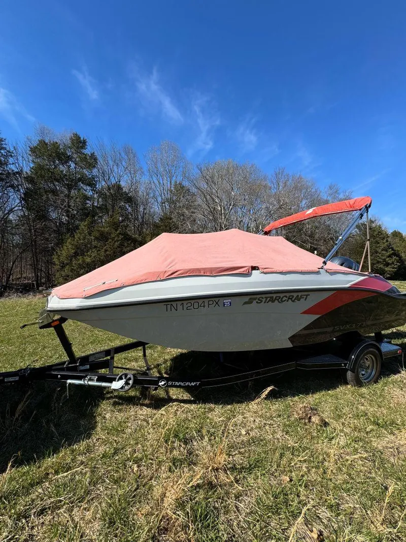 Slide: The Image of 2022 Starcraft SVX 171 OB boat with cover on trailer, parked on grassy field. - 7