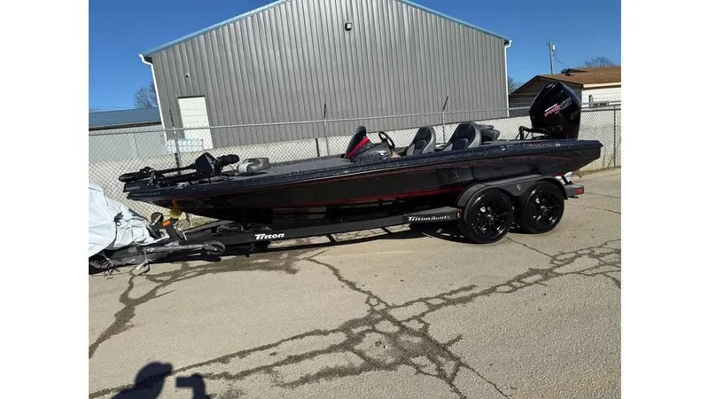 Slide: The Image of 2025 Triton 20XP Patriot boat on trailer, parked outdoors near a metal building. - 6