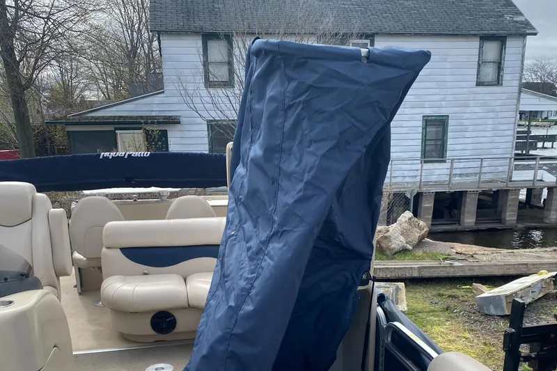 Slide: The Image of 2014 Godfrey 22 PF pontoon boat with blue cover, docked near a lakeside house. - 11