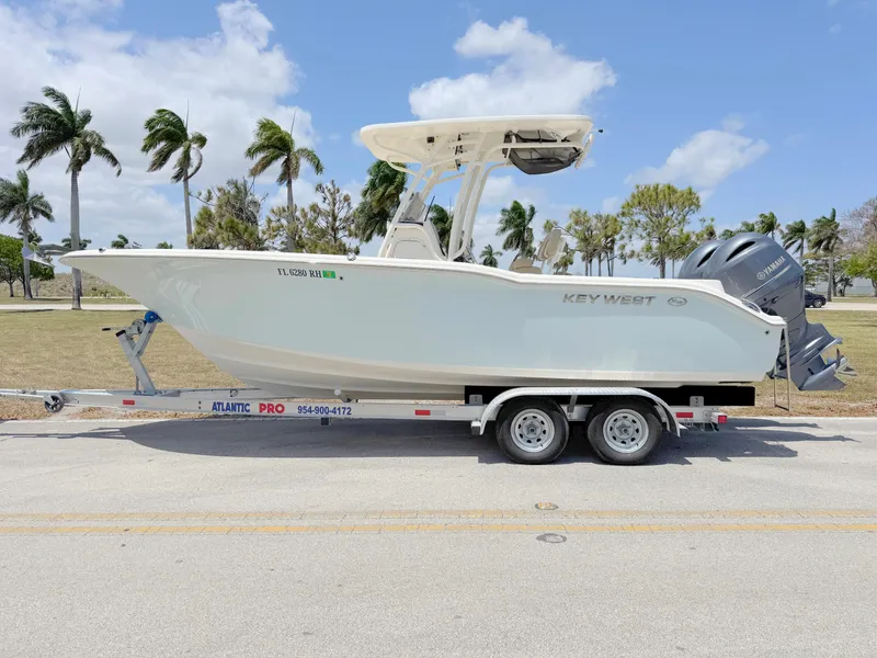 Slide: The Image of 2017 Key West 244 Center Console boat on trailer, parked roadside with palm trees in background. - 0