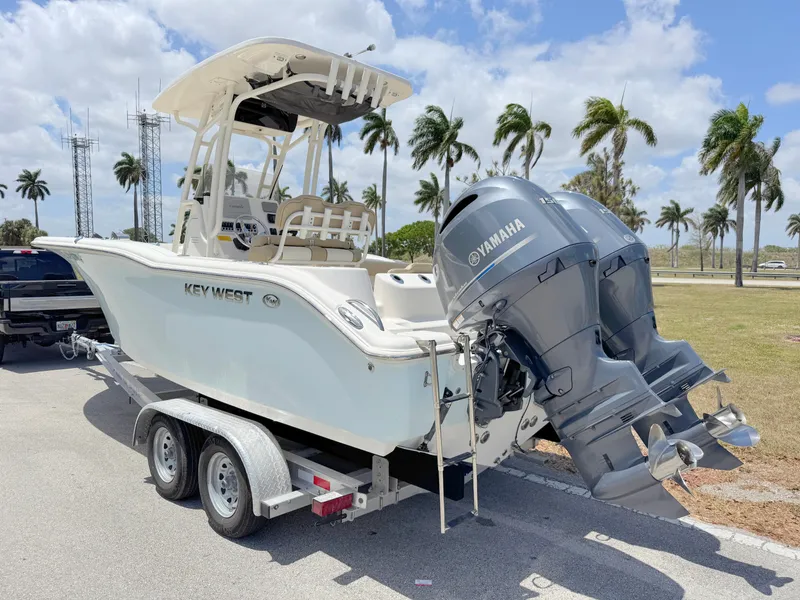 Slide: The Image of 2017 Key West 244 Center Console boat on trailer with twin Yamaha engines, parked near palm trees. - 2