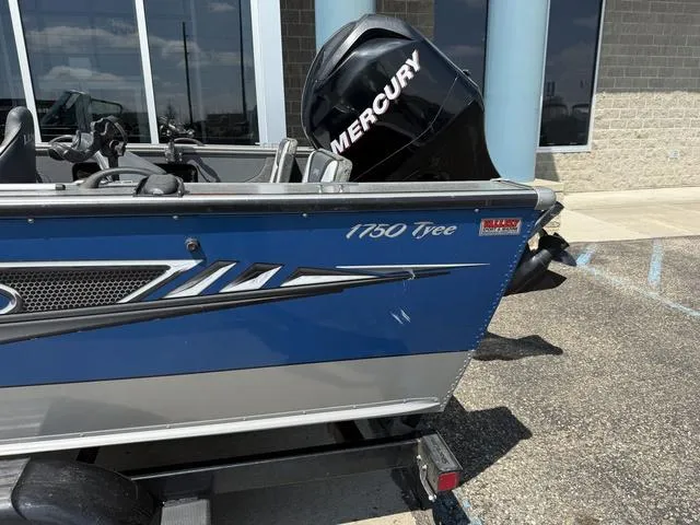 Slide: The Image of 2012 Lund 1750 Tyee boat with Mercury engine, parked outside a building. - 2