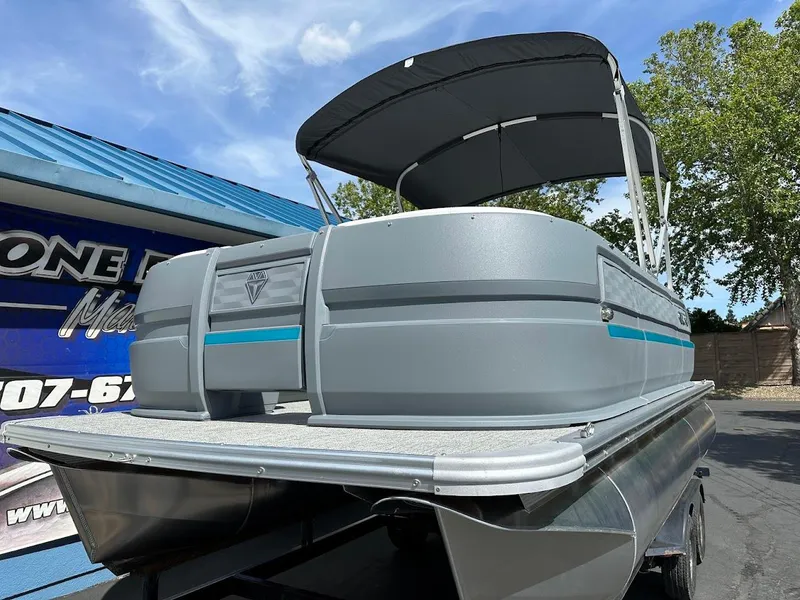 Slide: The Image of 2025 Aura Quad Lounge pontoon boat with canopy, parked outdoors under a blue sky. - 2