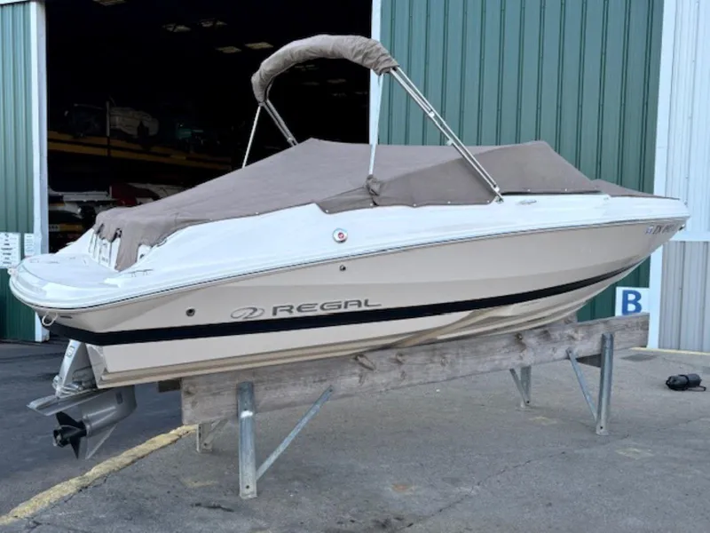 Slide: The Image of 2015 Regal 2000 ES boat with cover, stored on a stand outside a green building. - 28