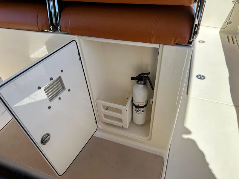 Slide: The Image of 2017 Scout 320 LXF boat storage compartment with fire extinguisher and brown seating. - 38