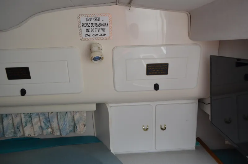 Slide: The Image of Interior of a 1996 Rinker 300 Fiesta Vee boat with storage cabinets and a humorous sign. - 32