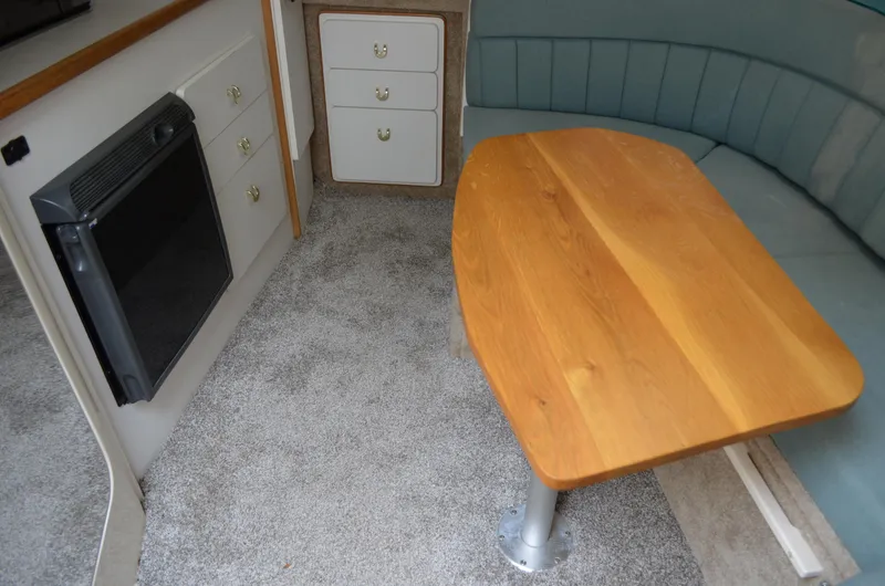 Slide: The Image of 1996 Rinker 300 Fiesta Vee interior with wooden table, cushioned seating, and compact kitchen area. - 36