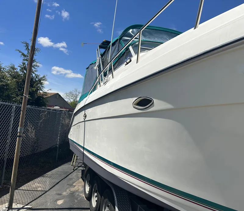 Slide: The Image of 1996 Rinker 300 Fiesta Vee boat on trailer, parked near chain-link fence under blue sky. - 7
