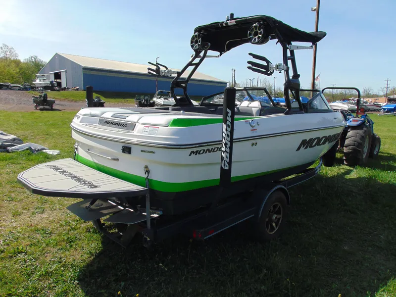 Slide: The Image of 2018 Moomba Mondo boat on trailer, green and white, parked on grass near a barn. - 9