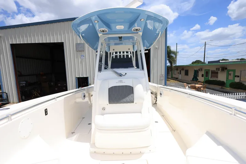 Slide: The Image of 2022 Cobia 301 Center Console boat with blue canopy, docked near industrial buildings. - 19