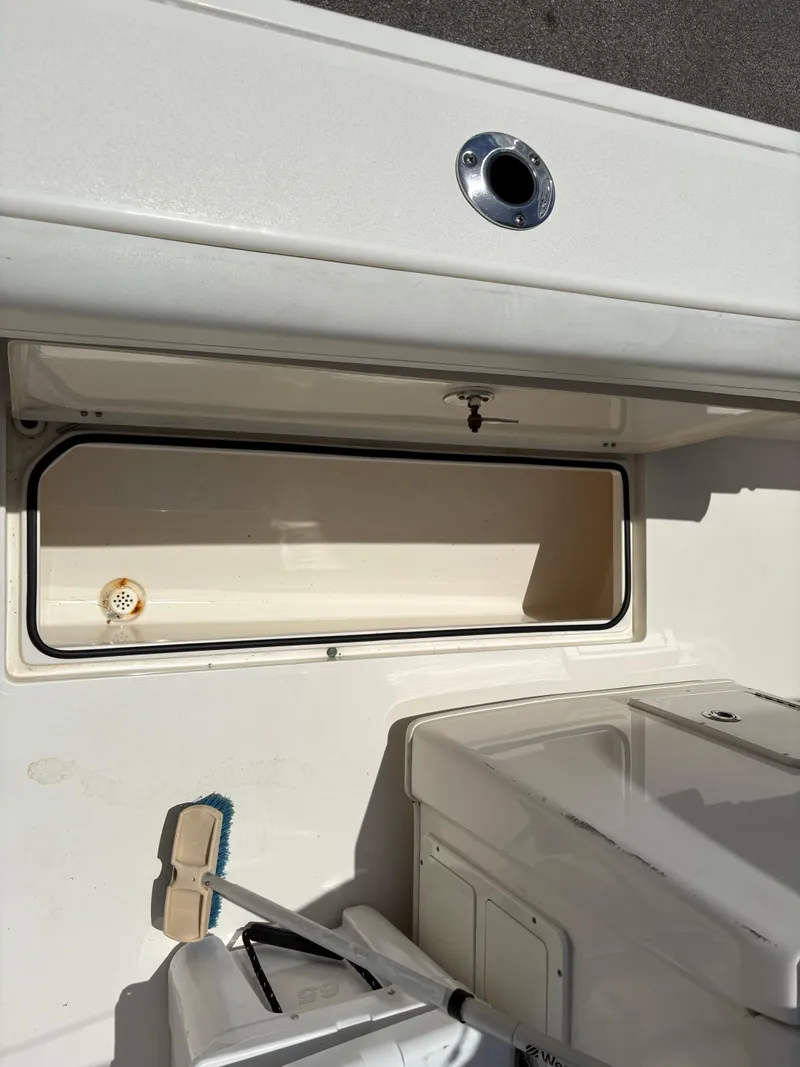 Slide: The Image of 2022 Cobia 301 Center Console boat storage compartment with cleaning brush. - 31