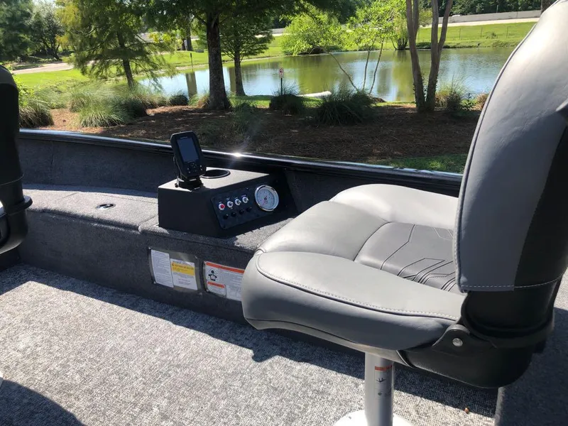 Slide: The Image of 2025 Tracker Super Guide V-16 T boat interior with gray seating and control panel by a lake. - 11