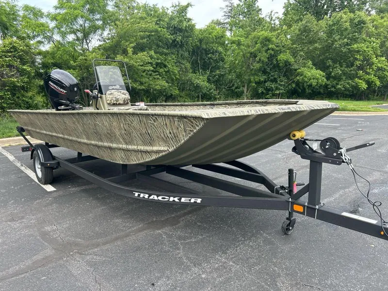 Slide: The Image of 2025 Tracker Grizzly 2072 CC boat on trailer, parked outdoors with lush greenery background. - 2