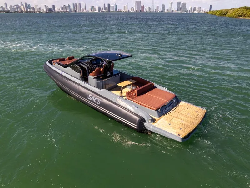 Slide: The Image of 2019 SACS Rebel 40 boat cruising on water with city skyline in background. - 2