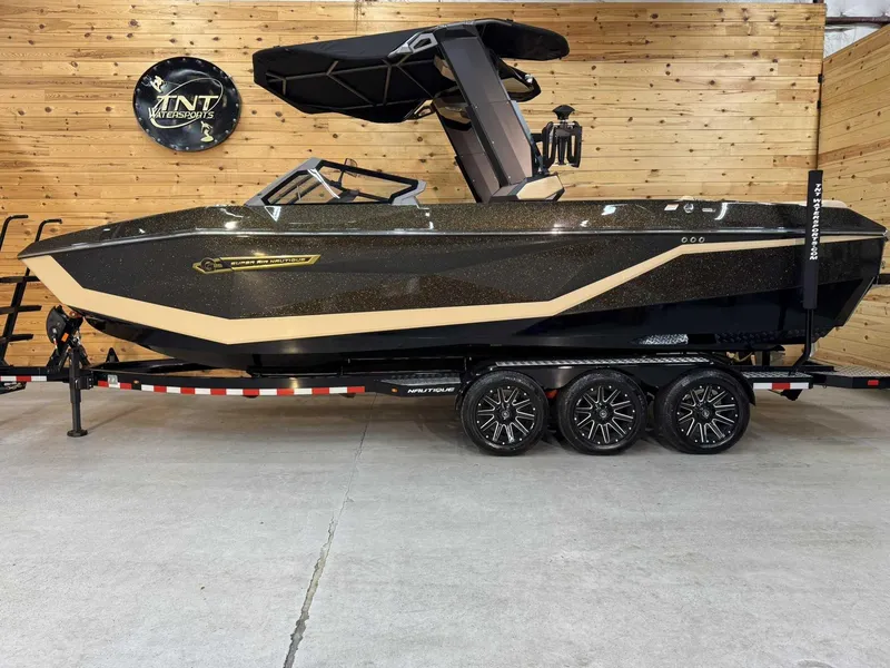 Slide: The Image of 2025 Nautique G25 boat on trailer in showroom, black and beige design. - 1