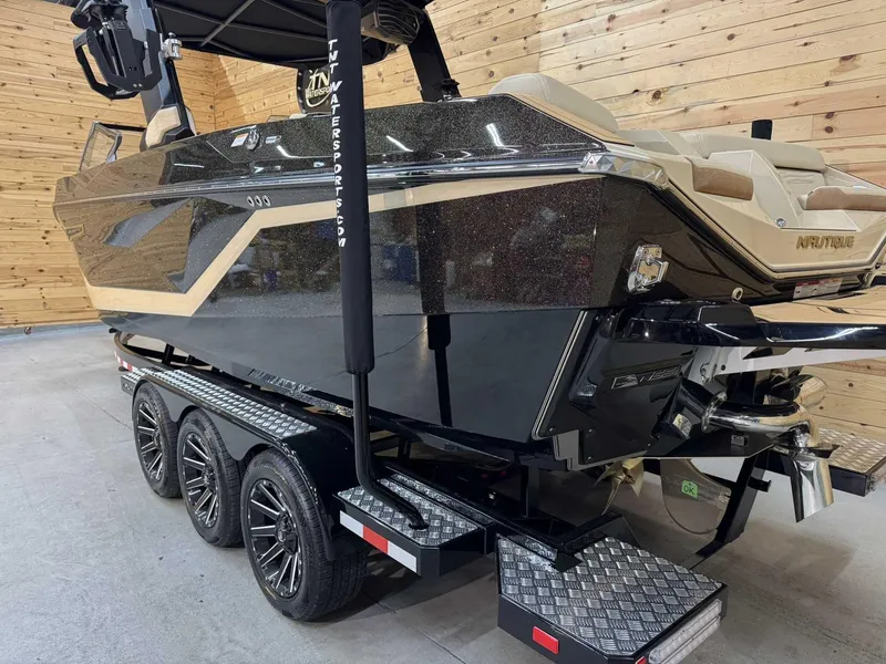 Slide: The Image of 2025 Nautique G25 boat on a triple-axle trailer in a wooden interior setting. - 2