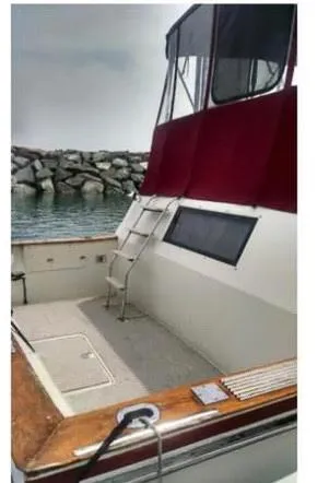 Slide: The Image of 1984 Wellcraft 44 Californian CMY yacht with red canopy, docked near rocky shoreline. - 15