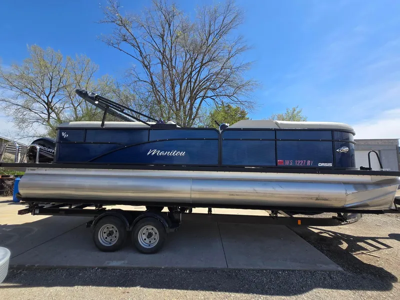 Slide: The Image of 2019 Manitou Oasis VP Tri Toon pontoon boat on trailer, parked outdoors. - 1