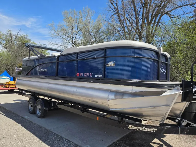 Slide: The Image of 2019 Manitou Oasis VP Tri Toon pontoon boat on trailer, parked outdoors. - 2