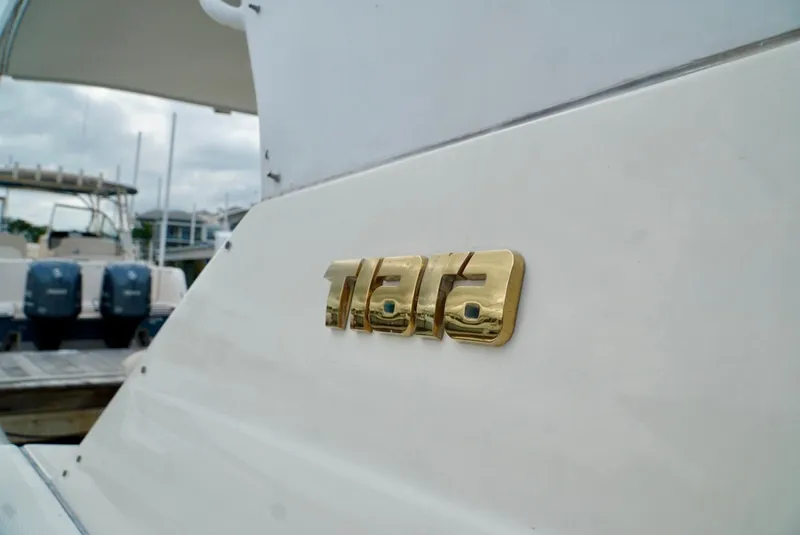 Slide: The Image of 1998 Tiara Yachts 4000 Express, gold logo detail, docked with outboard motors in background. - 14