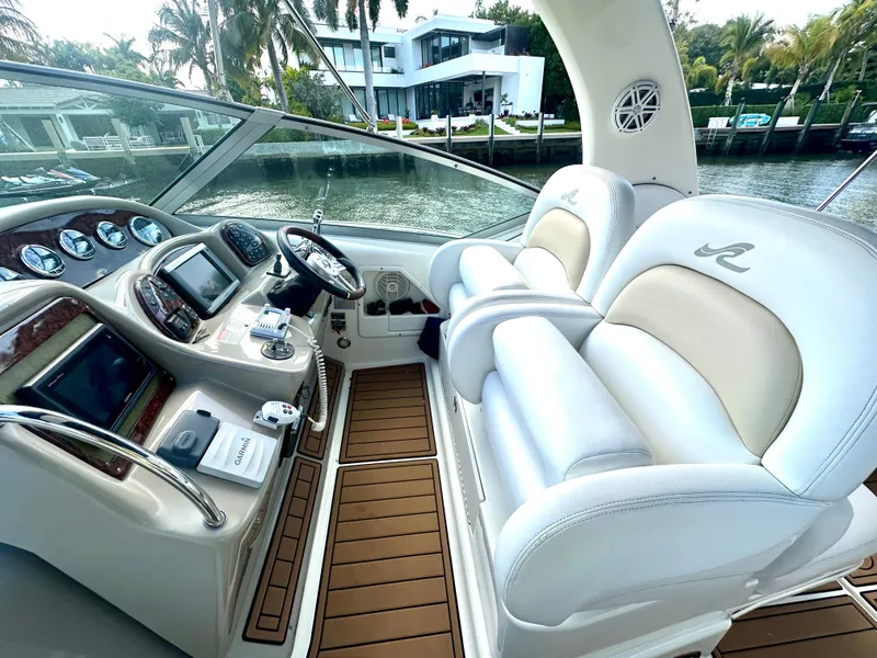 Slide: The Image of 2008 Sea Ray 420 Sundancer helm with luxurious seating and modern controls, docked by waterfront homes. - 32