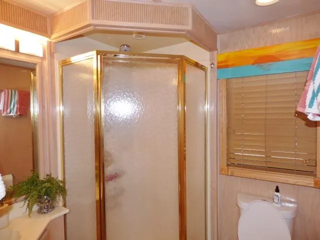 Slide: The Image of Bathroom with glass shower, wooden blinds, and decorative accents in a 2000 Stardust Cruisers 18x83. - 7