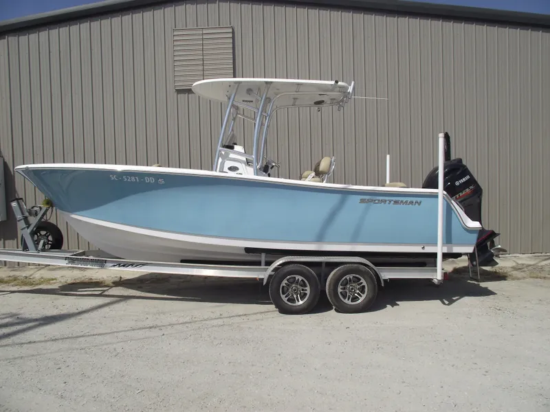Slide: The Image of 2016 Sportsman Open 232 Center Console boat on trailer, parked by a metal building. - 0