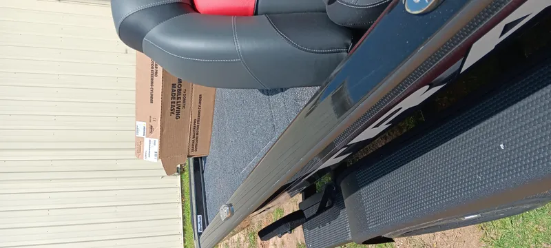 Slide: The Image of 2025 Tracker Savage 215 boat interior with black and red seating, cardboard boxes nearby. - 21