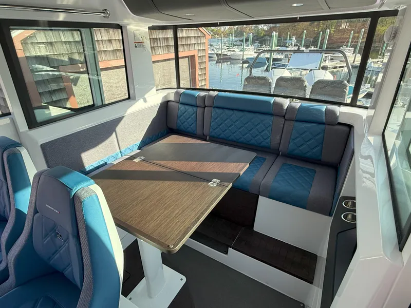 Slide: The Image of 2024 Axopar Cross Cabin interior with blue seating and wooden table, docked at marina. - 37