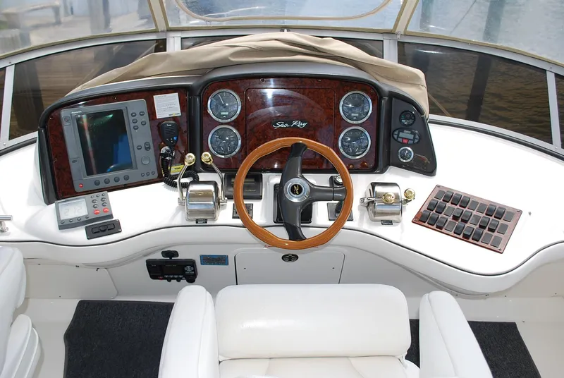 Slide: The Image of 2004 Sea Ray Sedan Bridge helm with wood accents, steering wheel, and navigation instruments. - 12