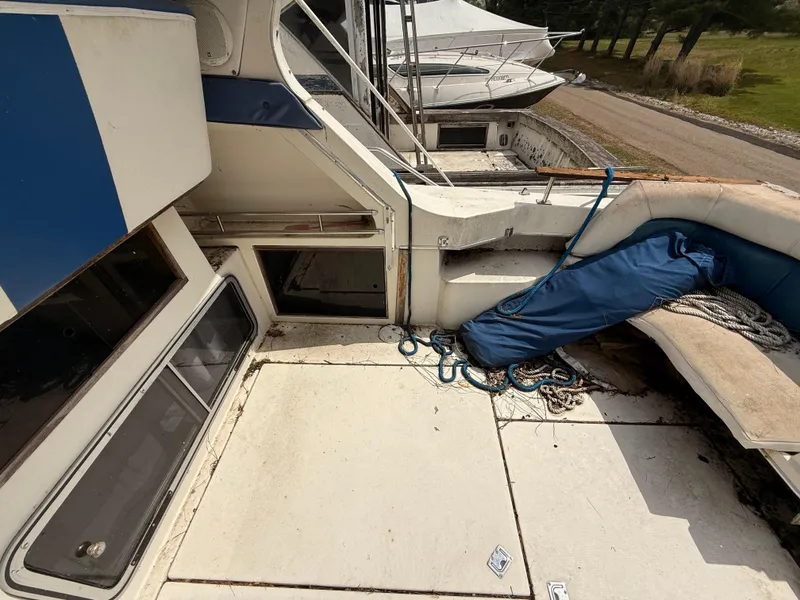 Slide: The Image of 1986 Cruisers 337 boat deck with ropes and blue cover, docked near a grassy area. - 7