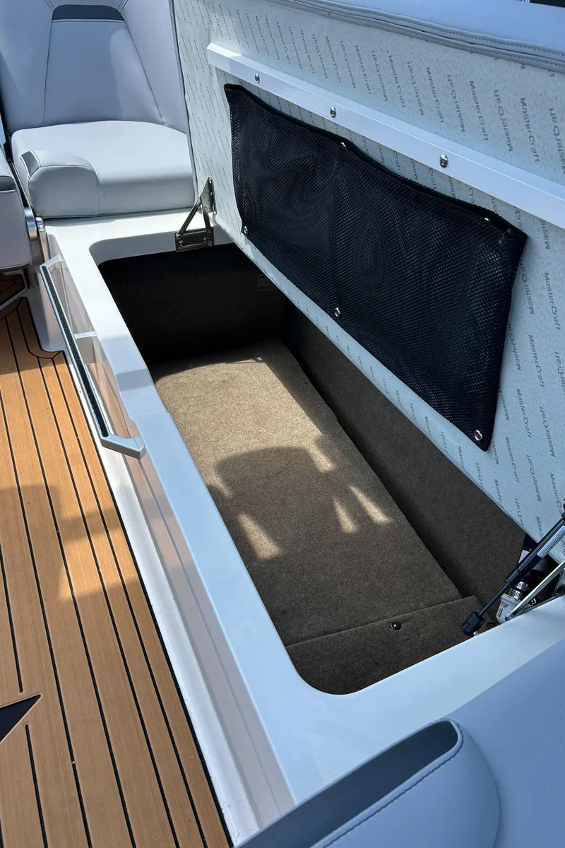 Slide: The Image of 2024 MasterCraft XStar S boat storage compartment with cushioned seating and teak flooring. - 7