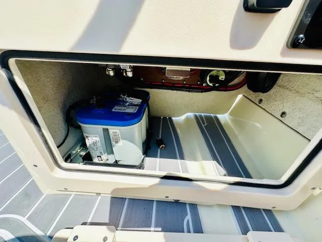 Slide: The Image of 1986 Boston Whaler 150 Sport storage compartment with battery, featuring striped flooring. - 28