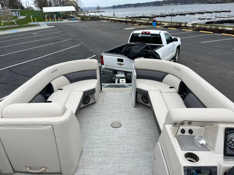 Slide: The Image of 2022 Harris Cruiser 230 pontoon boat interior with plush seating, parked near a lake. - 3