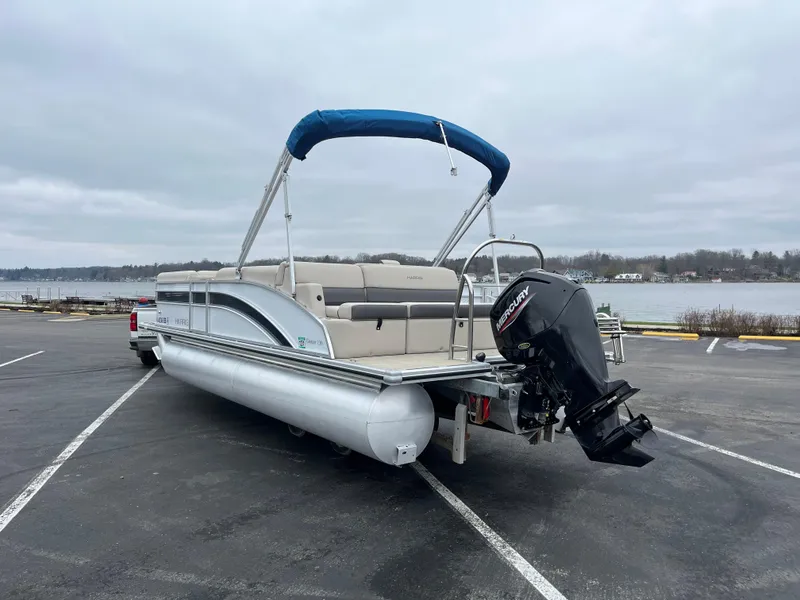 Slide: The Image of 2022 Harris Cruiser 230 pontoon boat with blue canopy on a trailer by a lake. - 9