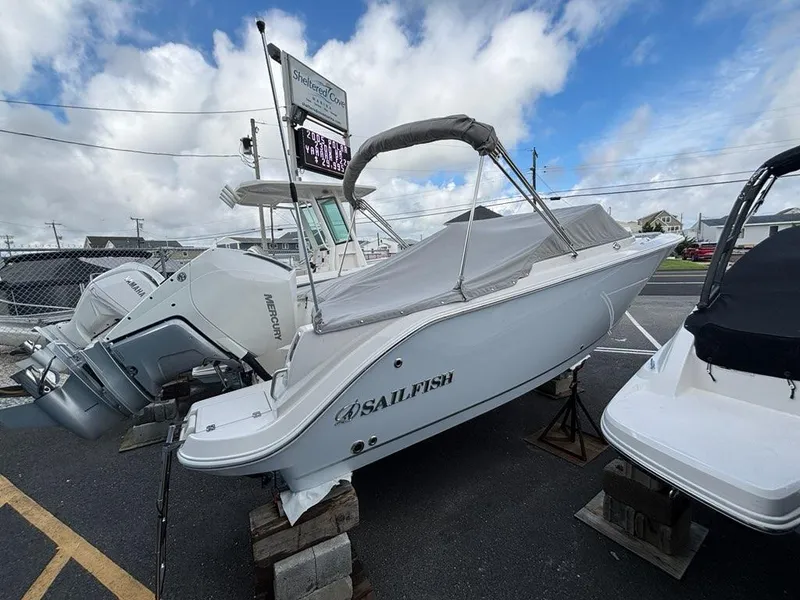 Slide: The Image of 2026 Sailfish 236 DC boat with Mercury engine, parked outdoors under cloudy sky. - 2
