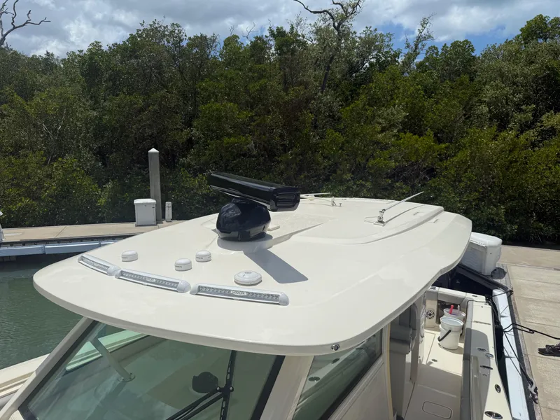 Slide: The Image of 2022 Scout 425 LXF boat roof with radar, docked near lush greenery. - 35